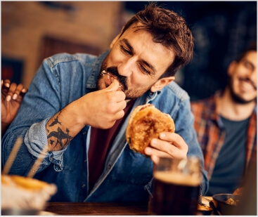 hungry-man-eating-burger-while-gathering-with-frie-2023-11-27-05-29-40-utc